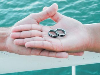 Cropped hands of couple holding rings against sea