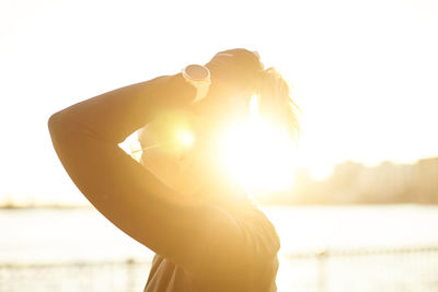 An athletic woman putting her hair up backlit by the sun.