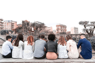 Multi ethnic young people sitting on a bench in a park, shot from behind their backs. wait concept