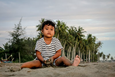 Happy boy sitting on sand at beach against sky