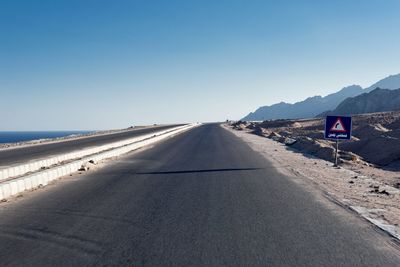 Road leading towards mountains against clear sky