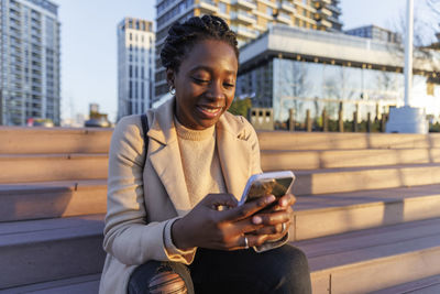 Smiling woman using smart phone on stairs at sunset