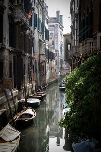 Boats moored in canal amidst buildings in city