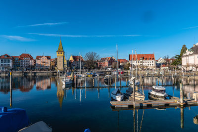 Sailboats moored in canal by buildings against blue sky