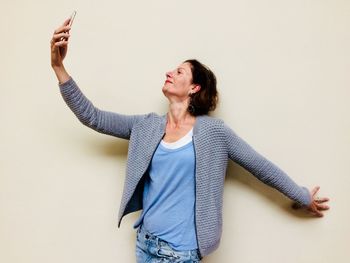 Mature woman taking selfie against beige background