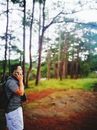 Side view of young man talking on mobile phone while standing in forest