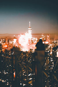 Rear view of man standing by illuminated buildings against sky at night