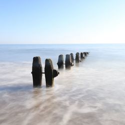 Wooden posts in sea against clear sky