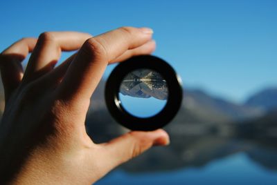 Cropped hand holding lens with upside down reflection of mountains