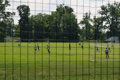 People playing soccer on field against trees