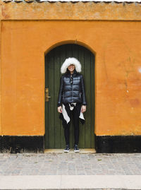 Full length portrait of woman standing against door