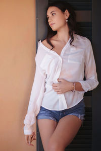 Portrait of young woman standing against wall