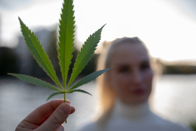 Close-up of woman holding marijuana against sky