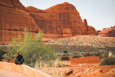 Woman sitting on retaining wall against rock formations