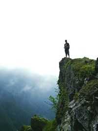 Man standing on mountain cliff against cloudy sky