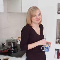 Smiling woman holding drink in mug while standing at kitchen