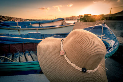 Close-up of hat and boat by sea against sky during sunset