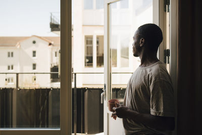 Side view of man looking out while having coffee at home