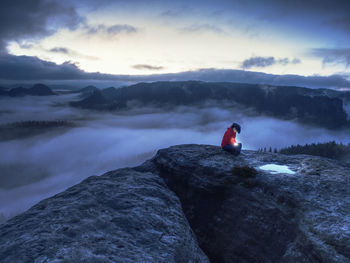 Woman in hands hold the sun. hiker girl sit in dark night above clouds and wait for sunrise. 