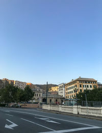 Road by buildings against clear blue sky