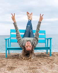 Mid adult woman sitting at beach against sky