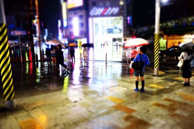 People walking on wet illuminated city at night