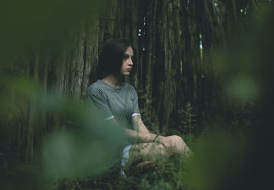 Thoughtful young woman sitting by tree in forest