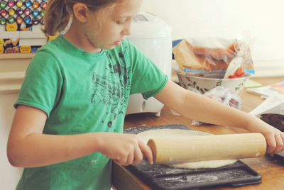 Girl rolling out dough at table in kitchen
