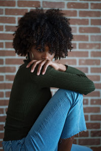 Beautiful black woman with afro hair sitting on the chair against the brick wall background