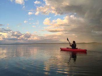 Mature woman canoeing on sea against cloudy sky during sunset