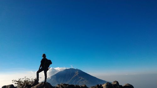 Rear view of man standing on rock against mountain and blue sky