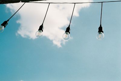 Low angle view of light bulbs hanging against blue sky