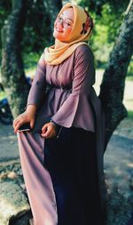 Portrait of young woman standing against trees