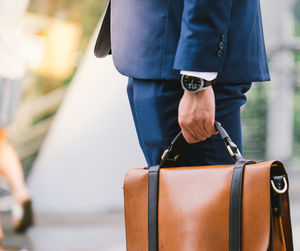 Midsection of businessman holding suitcase while standing outdoors