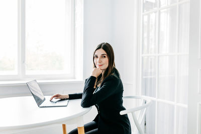 Side view of young woman using mobile phone while sitting on table