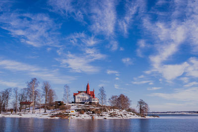 Lighthouse amidst buildings and sea against sky