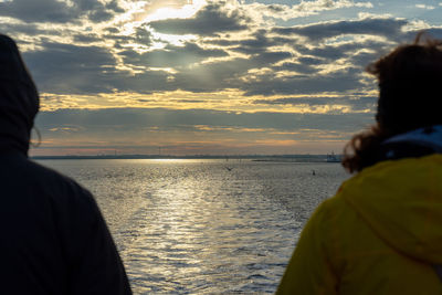 Rear view of couple on sea against sky during sunset