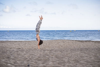Side view of woman practicing handstand at beach