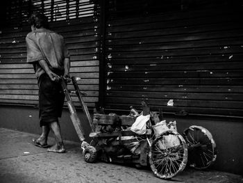 Homeless man pulling messy cart on sidewalk in city