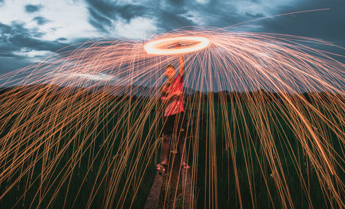 Low angle view of man spinning wire wool against sky during dusk