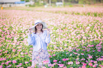 Portrait of smiling young woman wearing hat amidst flowerbed