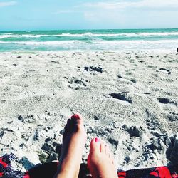 Low section of legs on beach against sky