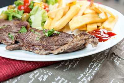 Close-up of grilled beef with french fries served on table