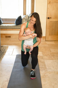 Happy mother carrying cute daughter while exercising on exercise mat at home