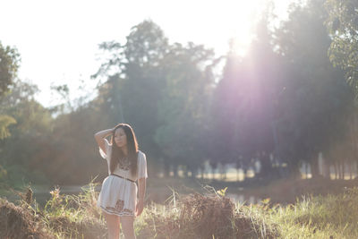 Portrait of young woman standing on grass against sky