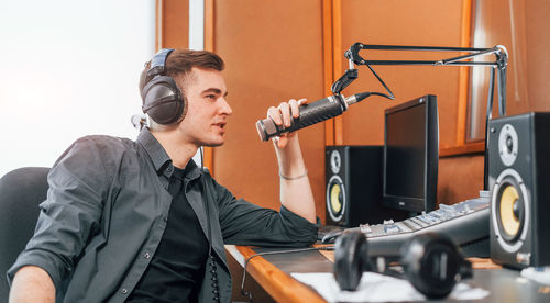 Talks and uses mic. young man is indoors in the radio studio is busy by broadcast.