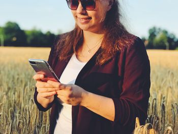 Young woman using mobile phone while standing on field