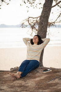 Woman with hands behind head leaning on tree