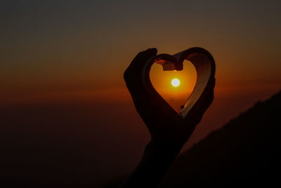 Silhouette person holding heart shape against sky during sunset