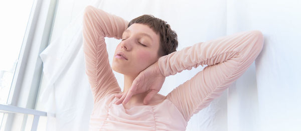 Side view of young woman with arms raised standing at home